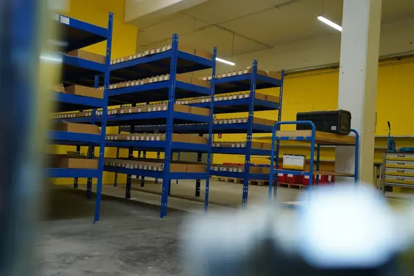 Blaue Metallregale mit Kartons stehen in einem gut beleuchteten Lagerraum mit gelber Wand.