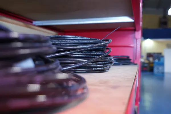 Schwarze Hydraulikschläuche liegen auf einem Holzregal in einer Werkstatt bereit.