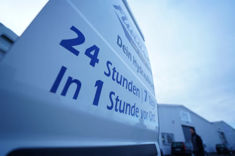 Ein Servicefahrzeug mit Aufschrift für 24-Stunden-Hydraulik-Notdienst vor einer Werkstatt.